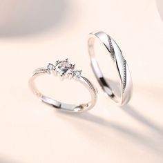 two white gold wedding rings with diamond accents on a light background, one is slightly open and the other is closed