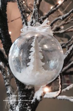 a glass ornament hanging from a tree with snow on it's branches