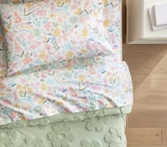 a bed with floral sheets and pillows on top of it next to a night stand