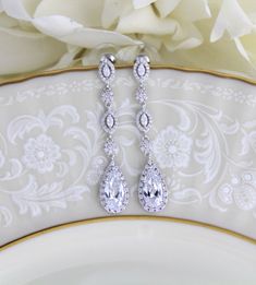 a pair of diamond earrings sitting on top of a white plate next to a flower