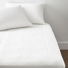 a white bed with two pillows on top of it next to a wall and wooden floor