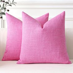 two pink pillows sitting on top of a white couch next to a potted plant