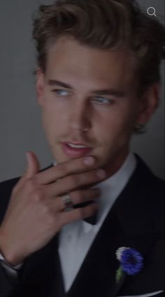 a young man in a tuxedo is holding his finger to his mouth and looking at the camera