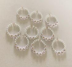 six pairs of pearl hoop earrings on a white tablecloth with pearls and gold beads