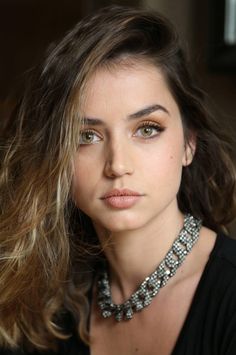 a woman with long hair wearing a necklace and black top is looking at the camera