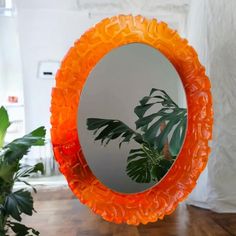 an orange mirror sitting on top of a wooden floor next to a potted plant