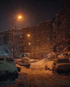 cars covered in snow parked on the side of a road at night with street lights