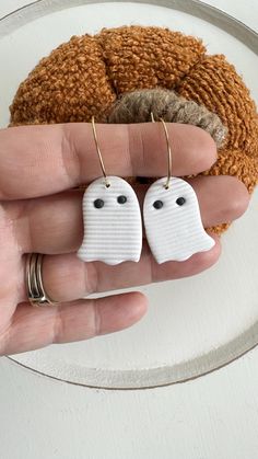 two small white ghost earrings sitting on top of a plate next to a brown pumpkin