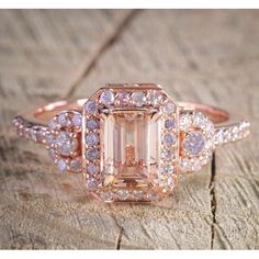 a fancy ring with an emerald surrounded by white and pink diamonds on a piece of wood