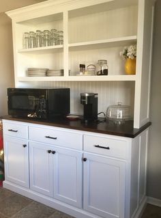 a kitchen with white cabinets and black counter top, microwave on the wall above it