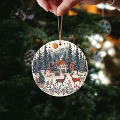 a hand holding a christmas ornament in front of a christmas tree with deer