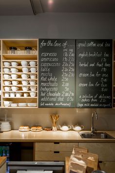 two chalkboard menus on the wall above a kitchen counter with dishes and cups