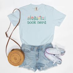 Featuring the words "Book Nerd" in a timeless typewriter font, this Comfort Colors T-shirt celebrates a reader's love of literature in style. Pretty flowers adorn the text making it as stylish as it is soft and comfy. This cute book shirt is a perfect addition to any book lover's wardrobe.! Want to spend every day in the comfort of Saturday morning? Slip on a Comfort Colors 1717 Adult Tee and enjoy the softness of 100% USA-grown ring-spun cotton. The fabric is garment-washed until it's as cozy as if you had worn it fifty times. Available Sizes: S-4XL Pigment Dye Colors: These colors provide a vintage look that will remain for the life of the garment Material: 100% Ring Spun US Cotton, Pre-Shrunk Fit: Relaxed Care: Machine Wash Cold Summer Bookish T-shirt With Letter Print, Bookish Cotton T-shirt With Letter Print, Summer Graphic Print Bookish T-shirt, Bookish Cotton T-shirt With Funny Print, Literary Cotton Relaxed Fit T-shirt, Literary Style Cotton T-shirt With Relaxed Fit, Bookish Cotton T-shirt With Slogan, Bookish Short Sleeve T-shirt For Spring, Literary Cotton T-shirt With Text Print