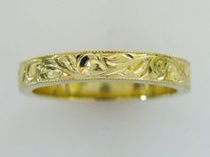 a yellow gold wedding ring with leaves and scrolls on the sides, set against a plain white background