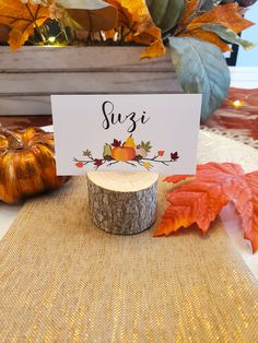 there is a place card on top of a tree stump with fall leaves around it