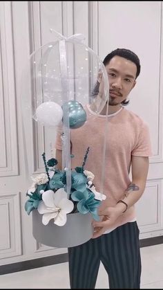 a man is holding a vase with flowers and balloons on it in front of his face