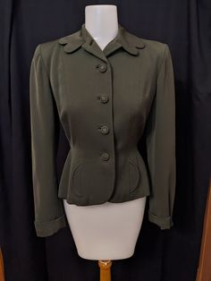 40s Wool gabardine jacket with some very charming details, like a scalloped collar, small circular faux pocket flaps, and a back trim with buttons and little pleats.  The jacket itself is well made with bound buttonholes, a full rayon crepe lining, and lots of seaming for a nice fit.  Green is hard to photograph, so I would say the actual color is a deep olive or bottle green.  In excellent condition, the jacket is a size 2. Measurements are approx: 15" across padded shoulders 34" bust 25" waist Fitted Collared Blazer With Buttons, Solid Blazer With Buttons For Tailoring, Collared Blazer With Button Closure, Collared Blazer With Button Closure For Tailoring, Fitted Solid Blazer With Button Cuffs, Fitted Solid Color Blazer With Button Cuffs, Vintage Tailored Outerwear With Buttons, Vintage Fall Blazer With Covered Buttons, Tailored Vintage Outerwear With Buttons