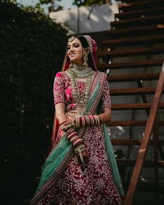 a woman in a red and green bridal outfit standing on stairs with her hands behind her back