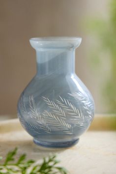 a blue glass vase sitting on top of a table next to a green leafy plant