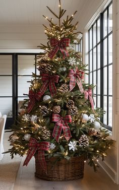 a decorated christmas tree with red and white bows in a basket on the floor next to a window