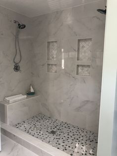 a bathroom with white marble and black dots on the floor, shower head, and bathtub