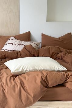 an unmade bed with brown sheets and pillows on top of it in front of a mirror