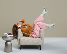 a woman laying on top of a white chair next to a table with a cell phone