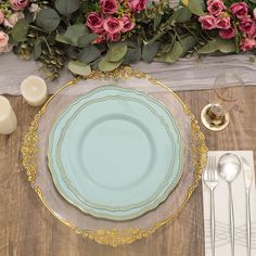 a blue plate with gold trim sits on a wooden table surrounded by flowers and candles