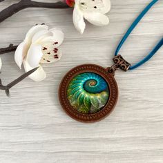 Turquoise blue wooden pendant necklace with fossil detail ammonite picture necklace. Cabochon jewellery, necklaces for women in the UK. This beautiful necklace is a round antique bronze tone  base which I've set with an emerald green ammonite fossil print glass cabochon,  it would make a perfect gift, maybe for a  birthday present. Its set on an 18 inch bright emerald green vegan suede cord, and fastens with a lobster clasp and extender chain. Gifts - If this item is a gift, please select 'gift Artistic Turquoise Necklace With Large Pendant, Bronze Cabochon Necklace For Gifts, Artistic Turquoise Necklace Gift, Artistic Turquoise Necklace With Round Pendant, Nature-inspired Cabochon Round Pendant Jewelry, Unique Blue Spiral-shaped Jewelry, Nature-inspired Round Cabochon Pendant Jewelry, Blue Nature-inspired Round Pendant Necklace, Handmade Turquoise Spiral Jewelry