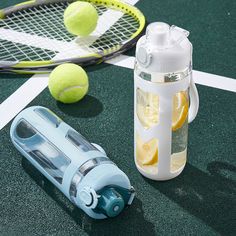 two tennis rackets and a water bottle on the ground next to some tennis balls