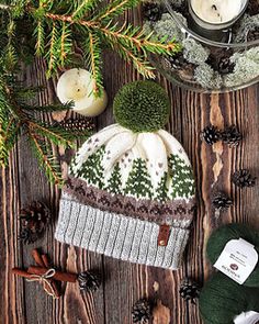 a knitted hat sitting on top of a wooden table next to pine cones and candles