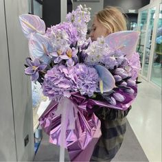 a woman holding a bouquet of purple flowers and butterflies in front of an airport door