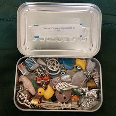 a metal container filled with lots of different types of beads and charms on top of a green surface