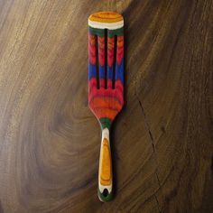 a wooden comb with multicolored designs on it sitting on a wood table top