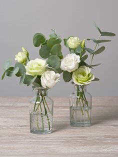 two clear vases with white and green flowers in them