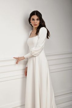 a woman in a white dress leaning against a wall with her hand on the side