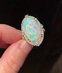 Gorgeous, mesmerizing Ethiopian opal cabochon of AAA quality is framed by dainty diamonds and four blue topazes on each side. The opal sparkles, showcasing streaks and circles of pink, deep blue colors, neon and yellow hues. A truly breathtaking stone! Four soft baby blue round faceted cut topazes add nice detail to the ring. In addition to the frame, diamonds are also placed on the split top part of the band adding more glamour and shine. Very beautiful and elegant ring! We also offer matching Luxury Handmade Yellow Gold Opal Ring, Luxury Ethiopian Opal Engagement Ring, Luxury Adjustable Opal Ring Gift, Luxury Adjustable Opal Ring As Gift, Luxury Cabochon Opal Ring For Engagement, Big Opal Ring, Luxury Gold Opal Ring With Diamond Accents, Luxury Oval Cabochon Opal Ring For Formal Occasions, Luxury Opal Ring With Diamond And Gemstone Accents