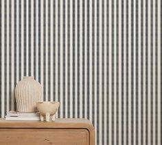 a white vase sitting on top of a wooden dresser next to a striped wallpaper