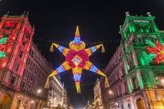 the christmas lights are on all sides of the buildings in the city square, and there is a large star hanging from the ceiling