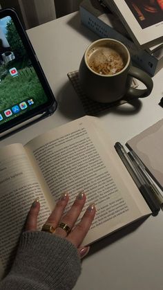 an open book sitting on top of a table next to a cup of coffee and cell phone