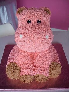 a cake shaped like a hippo sitting on top of a red table cloth covered in pink frosting