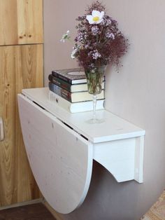 a white desk with flowers and books on it in front of a wooden cabinet next to a wall