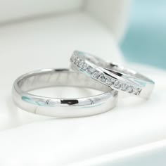 two wedding rings sitting on top of a white table next to each other with diamonds in them