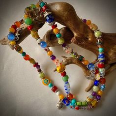 multicolored beaded bracelets are displayed on a piece of driftwood