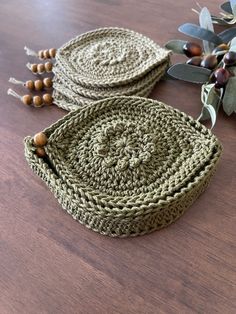 two crocheted baskets sitting on top of a wooden table next to leaves and berries