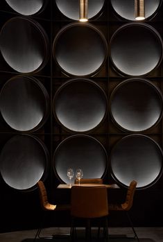 two chairs and a table with wine glasses on it in front of a dark wall