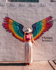 a woman standing in front of a wall with an angel painted on it's side