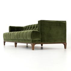 a green couch sitting on top of a white floor next to a wooden leg chair