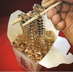 a person holding chopsticks over a box filled with gold coins