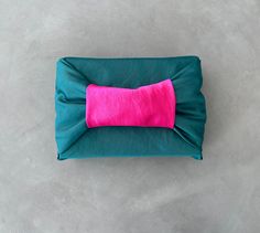 a green pillow with a pink bow on the top and bottom, sitting on concrete